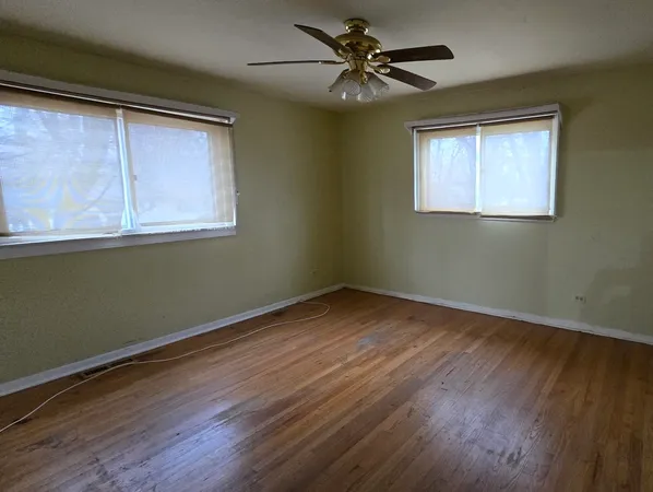 an empty room with wooden floor fan and windows