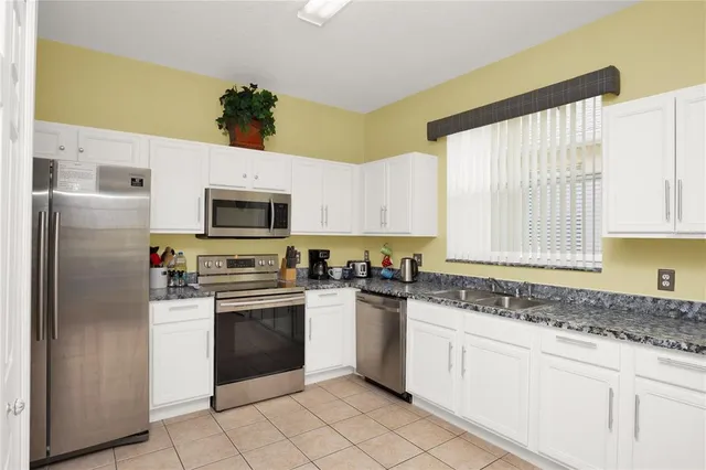 a kitchen with stainless steel appliances granite countertop white cabinets a sink a stove a microwave and a refrigerator