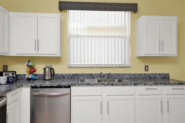 a kitchen with granite countertop white cabinets sink and window