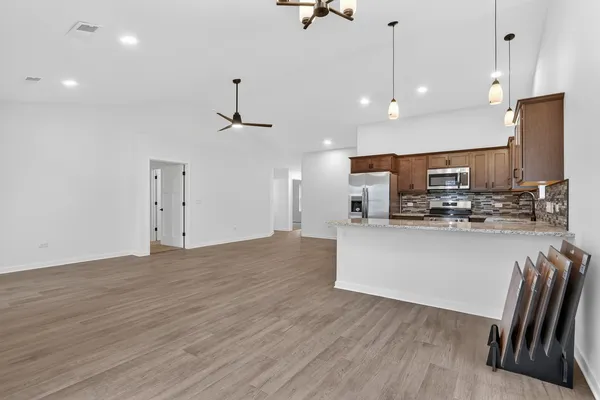a kitchen with stainless steel appliances granite countertop a refrigerator a stove a microwave oven a sink with island and chairs with wooden floor