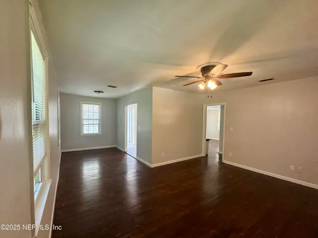 an empty room with wooden floor fan and windows