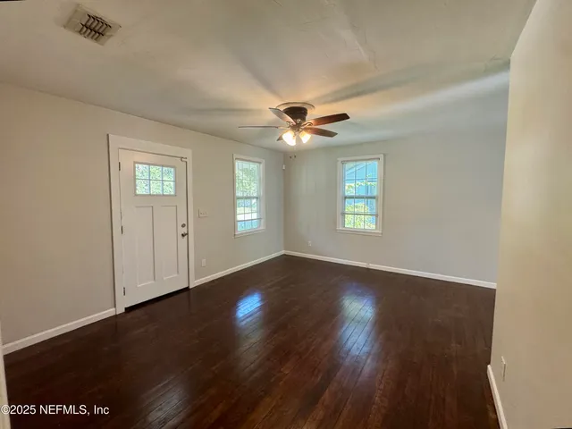 an empty room with wooden floor ceiling fan and windows