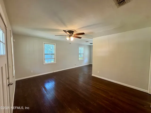 an empty room with wooden floor chandelier fan and windows