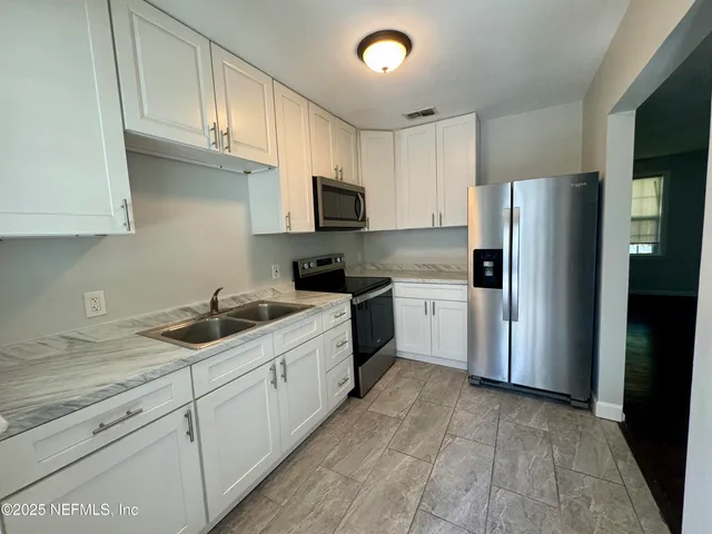 a kitchen with granite countertop a refrigerator sink and white cabinets