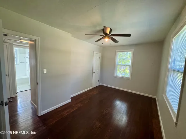 an empty room with wooden floor chandelier fan and windows