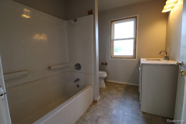 6577 East Deckerville Road Deford, MI 48729 - Photo 20 of 23 Bathroom featuring a white integrated shower and tub unit, a single vanity with a countertop, a window with natural light, and a toilet