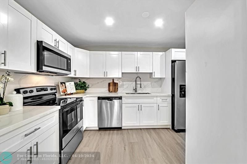 a kitchen with stainless steel appliances granite countertop a stove top oven a sink dishwasher and a refrigerator with wooden floor