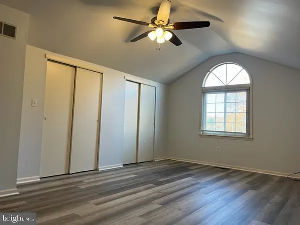 an empty room with wooden floor fan and windows