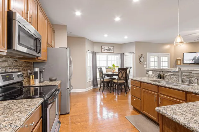 a kitchen with stainless steel appliances granite countertop a stove top oven a sink a dining table and chairs