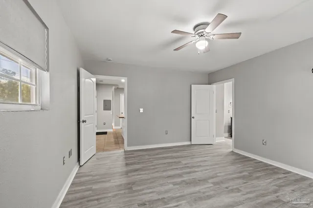 a view of an empty room with wooden floor and a ceiling fan