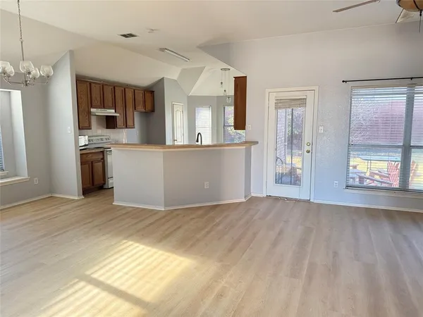 a view of an empty room with kitchen and window