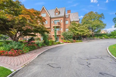 a view of a brick house with a small yard plants and a large tree