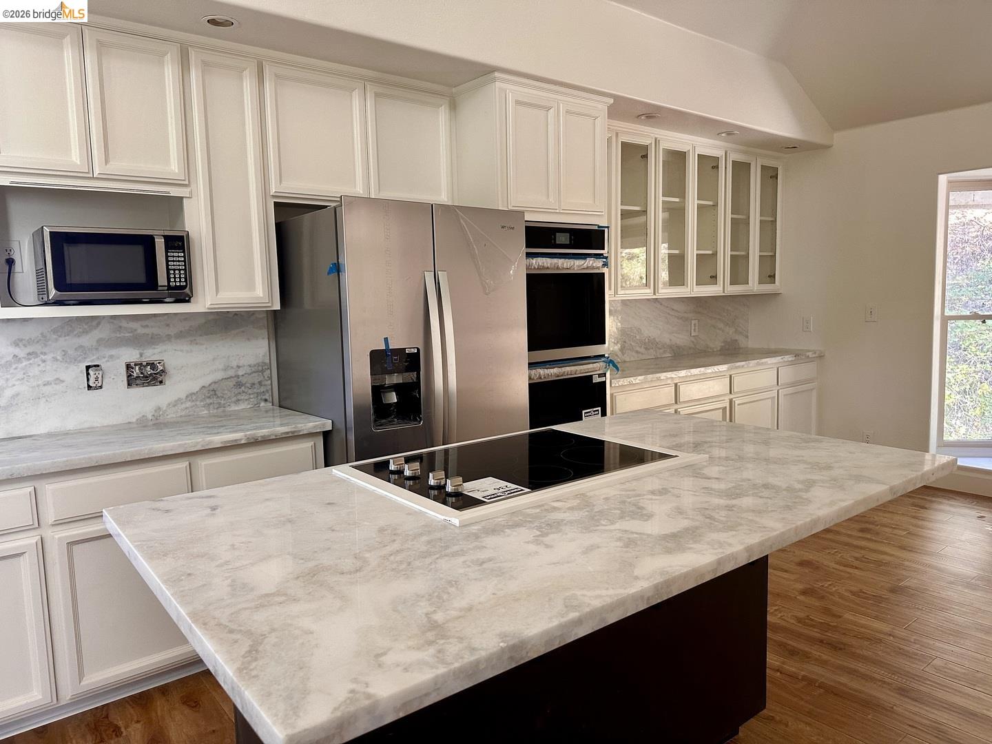 2080 Nelson Road Camino, CA 95709 - Photo 14 of 55 Kitchen featuring white shaker-style cabinetry, a large kitchen island with cooktop, stainless steel appliances, light-toned stone countertops, and wood-finish flooring