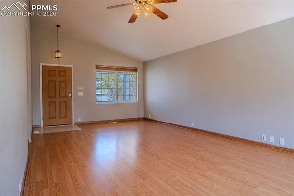 an empty room with wooden floor chandelier fan and windows
