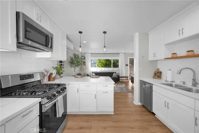 a kitchen with stainless steel appliances a sink dishwasher a stove top oven a refrigerator with wooden floor and cabinets