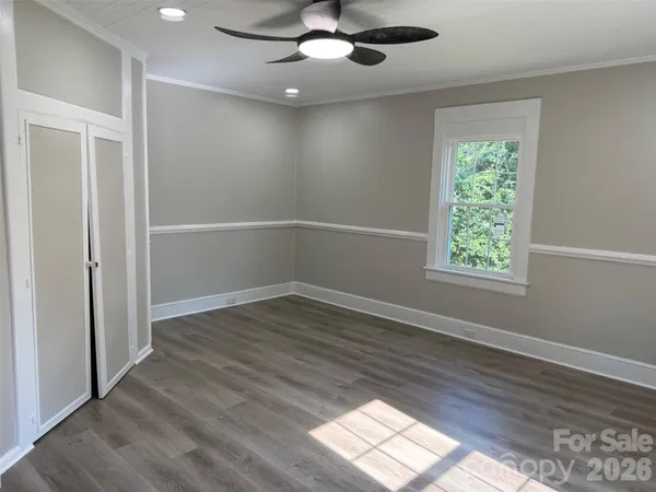 an empty room with wooden floor chandelier fan and windows