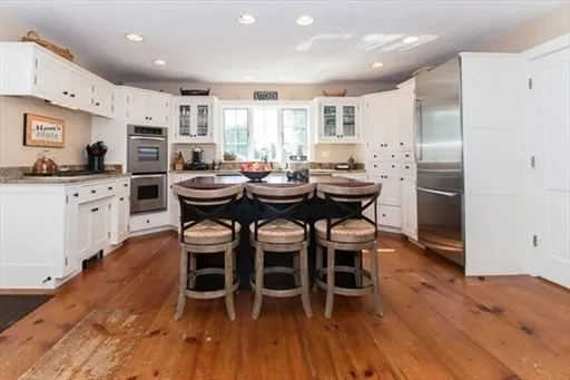 a kitchen with stainless steel appliances kitchen island granite countertop wooden floor and white cabinets