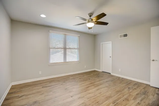 an empty room with wooden floor fan and windows