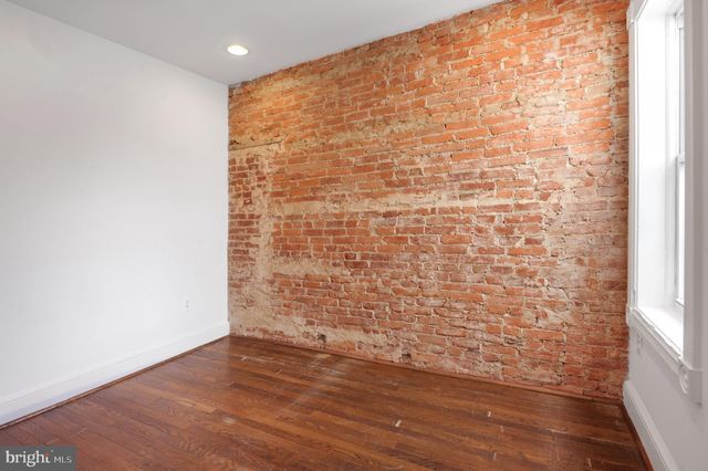 a view of empty room with wooden floor and brick walls