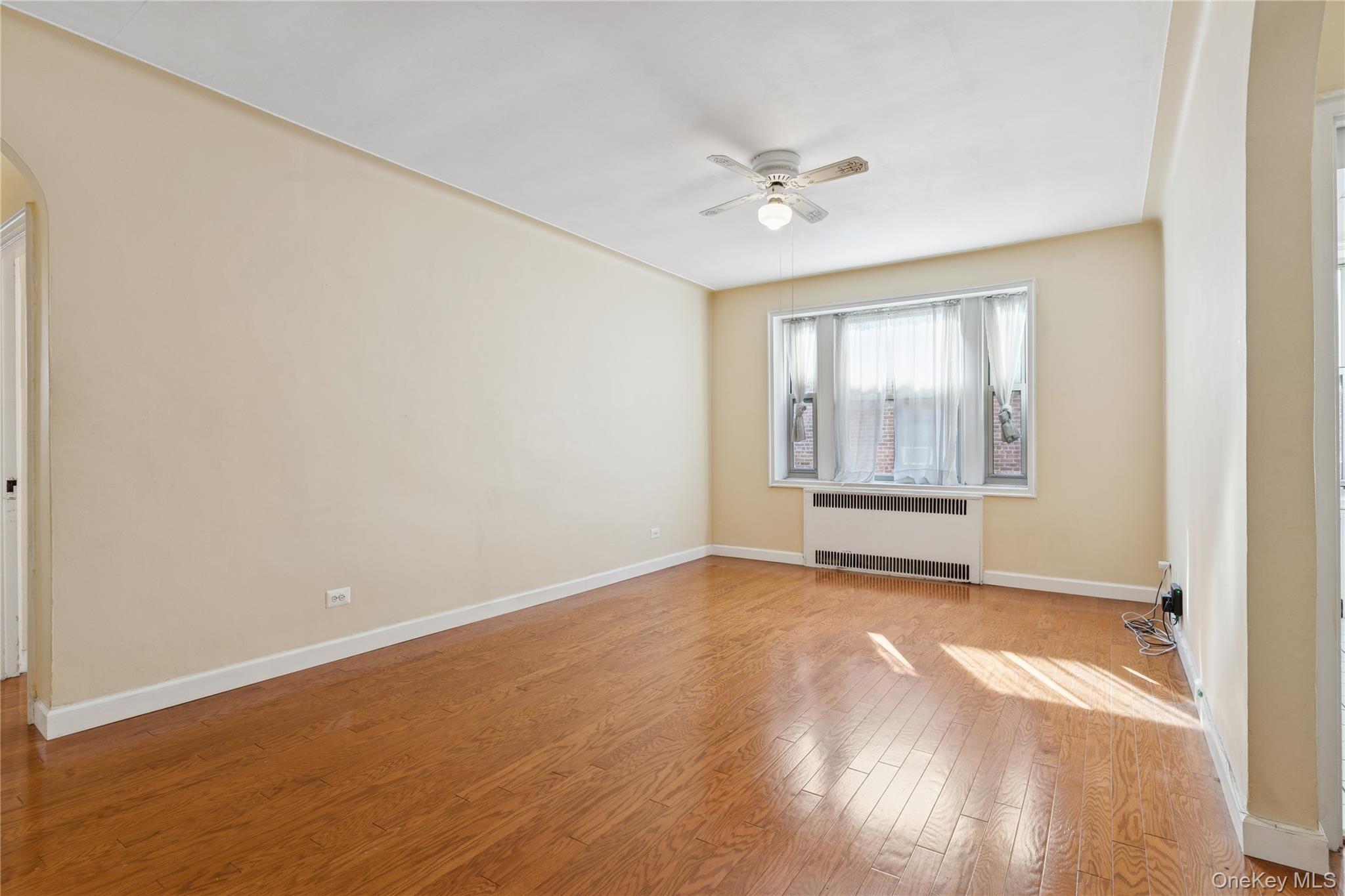 Unfurnished room featuring arched walkways, wood finished floors, radiator heating unit, and a ceiling fan