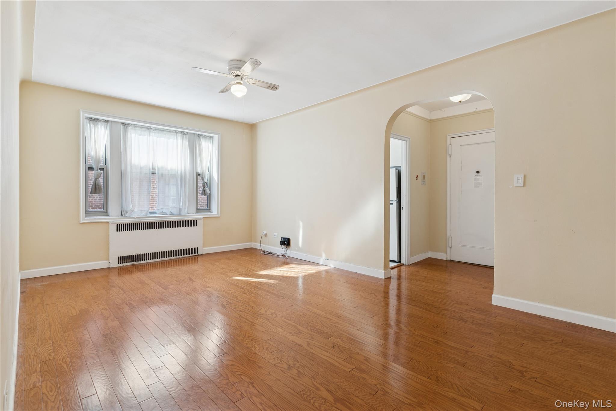 110-31 73rd Road, Unit 5N Queens, NY 11375 - Photo 4 of 13 Empty room with wood-type flooring, radiator, arched walkways, and a ceiling fan