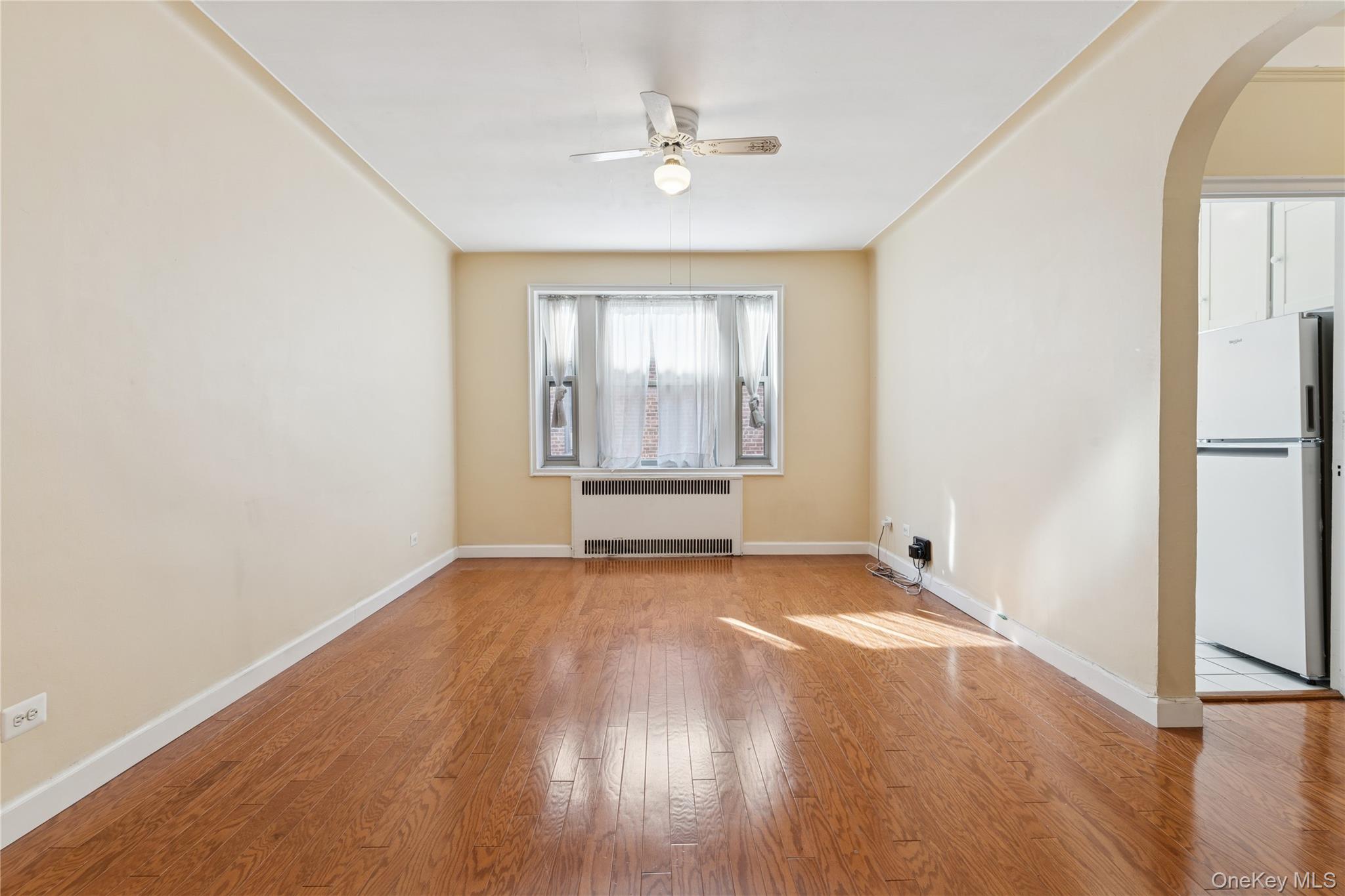 110-31 73rd Road, Unit 5N Queens, NY 11375 - Photo 5 of 13 Spare room with arched walkways, light wood-style flooring, ceiling fan, and radiator