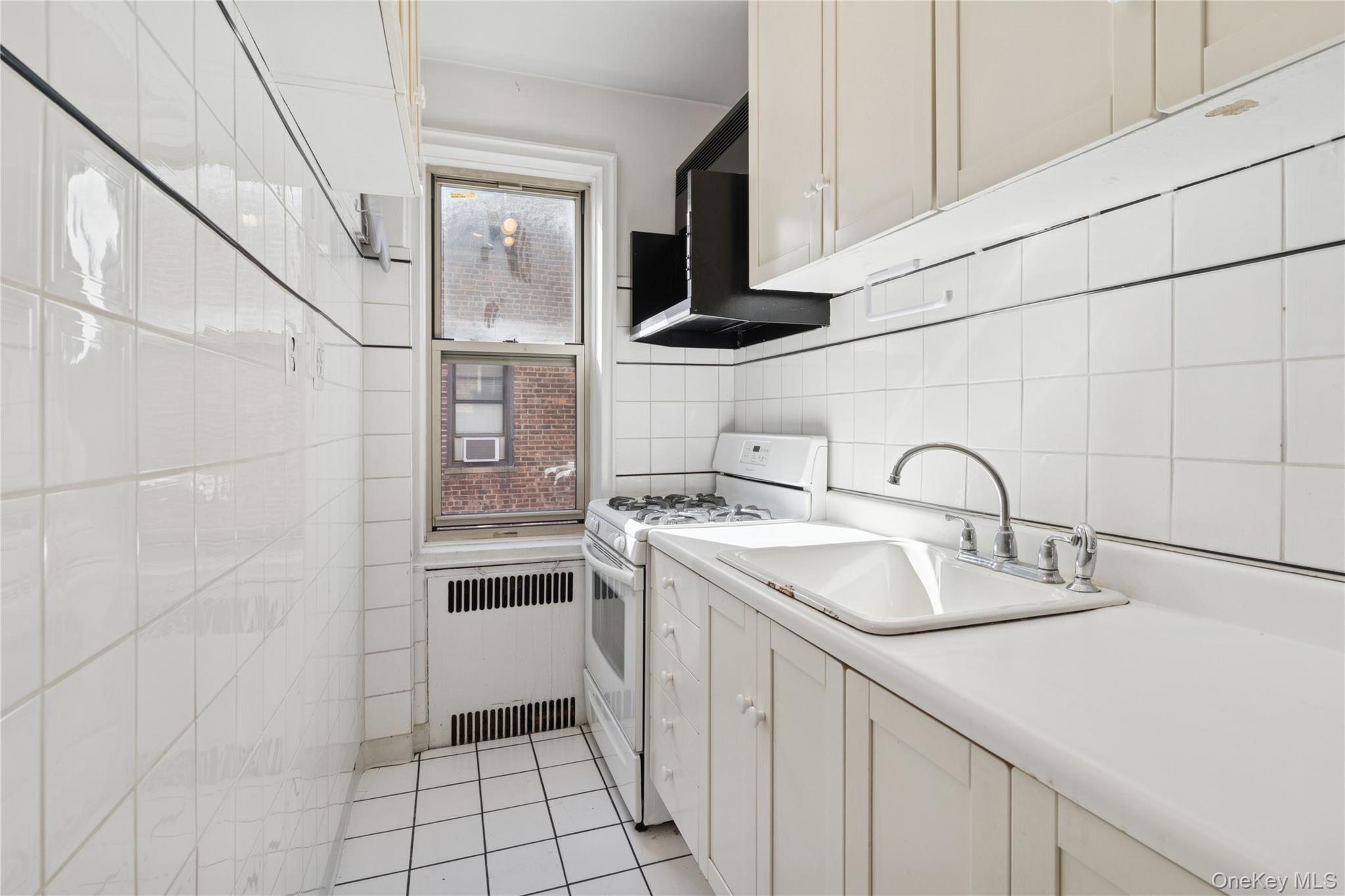 110-31 73rd Road, Unit 5N Queens, NY 11375 - Photo 6 of 13 Kitchen featuring white gas stove, radiator heating unit, light countertops, tasteful backsplash, and light tile patterned flooring