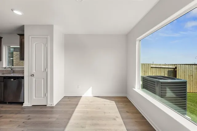 a view of a hallway to an empty room with wooden floor and a window