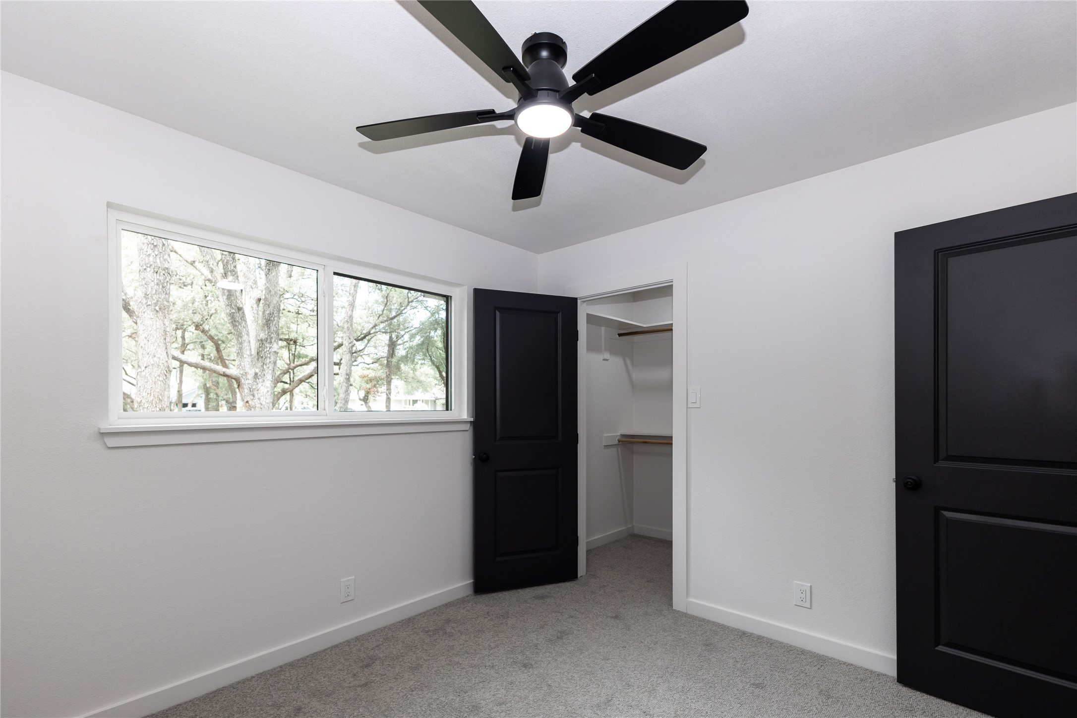 205 Bello Circle Georgetown, TX 78628 - Photo 21 of 36 A well-lit bedroom with modern dark doors, a large window overlooking trees, and comfortable gray carpeting.