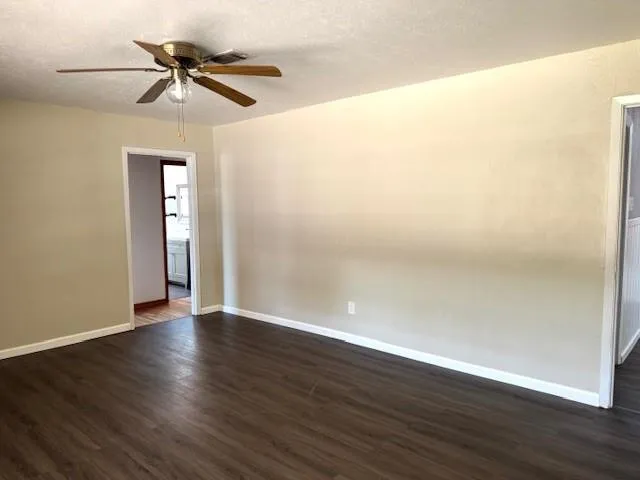 a view of an empty room with wooden floor and a ceiling fan