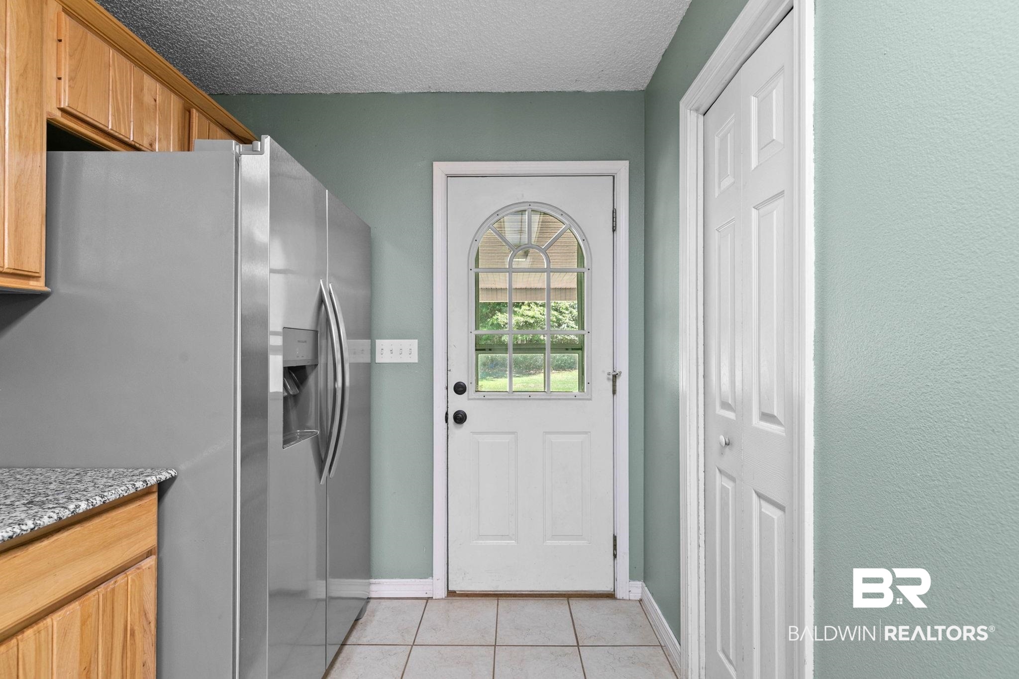20219 Greek Cemetery Road Robertsdale, AL 36567 - Photo 21 of 41 Entry door with arched window and decorative grid, paneled closet door, stainless steel refrigerator, granite-style countertop, and wood cabinetry