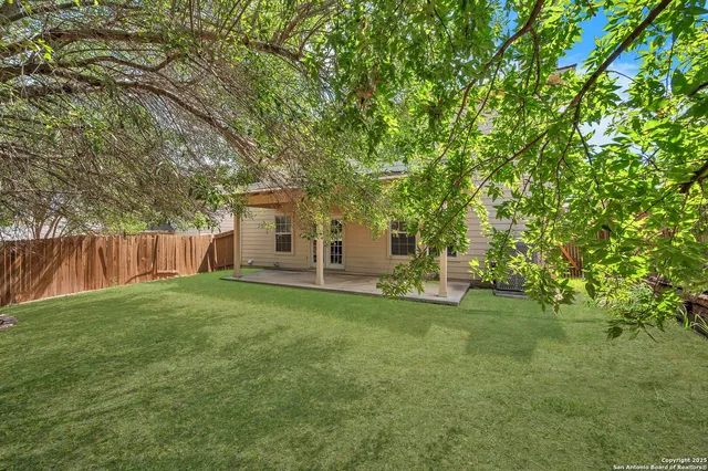 a backyard of a house with a large tree and wooden fence