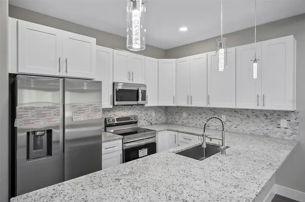 a kitchen with stainless steel appliances granite countertop a refrigerator a sink a stove and white cabinets