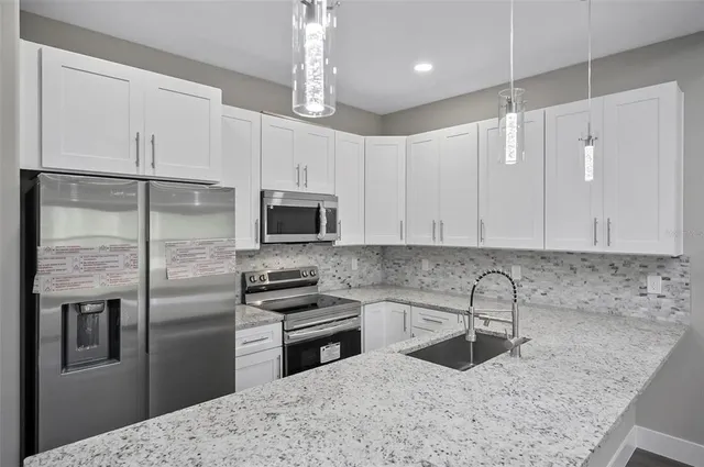 a kitchen with stainless steel appliances granite countertop a refrigerator a sink a stove and white cabinets