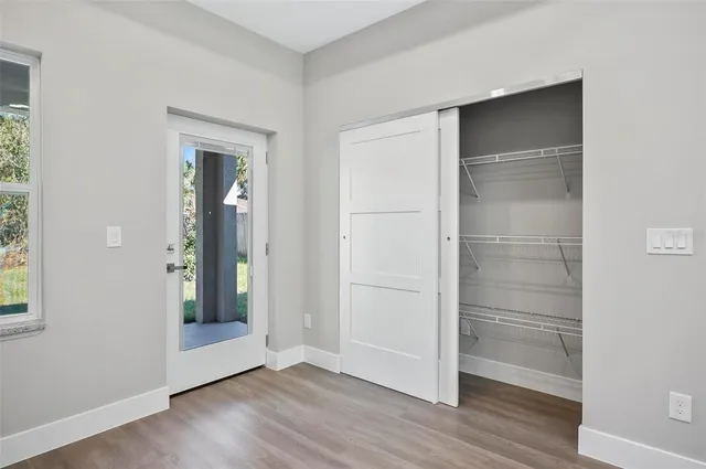 a view of an empty room with wooden floor & windows