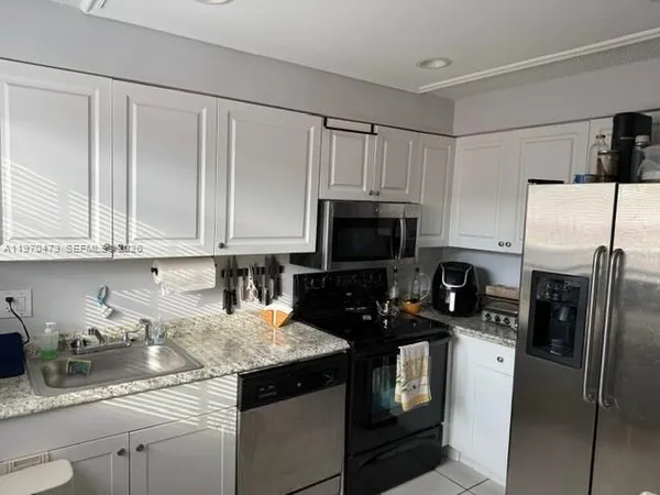 a kitchen with granite countertop white cabinets a refrigerator and a sink