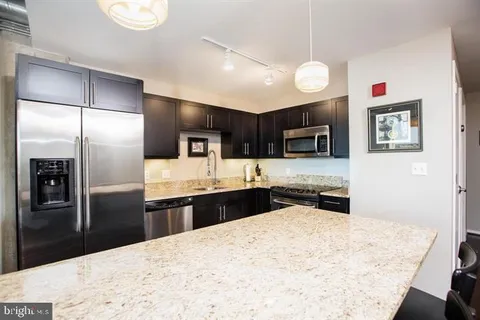 a kitchen with stainless steel appliances kitchen island granite countertop a refrigerator oven a sink with dishwasher and wooden cabinets
