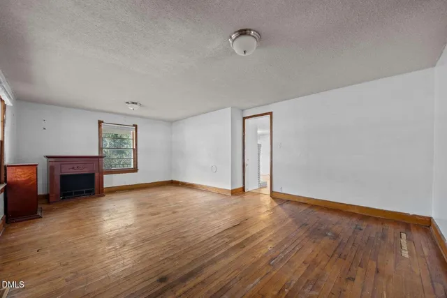 a view of an empty room with wooden floor and a fireplace