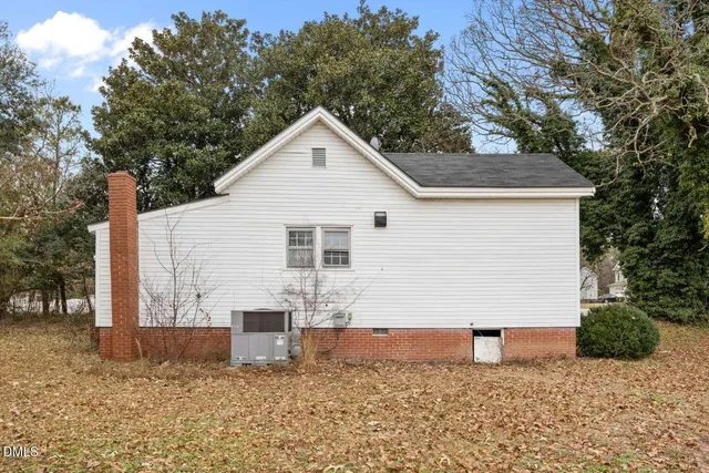 a view of a white house next to a yard with large trees