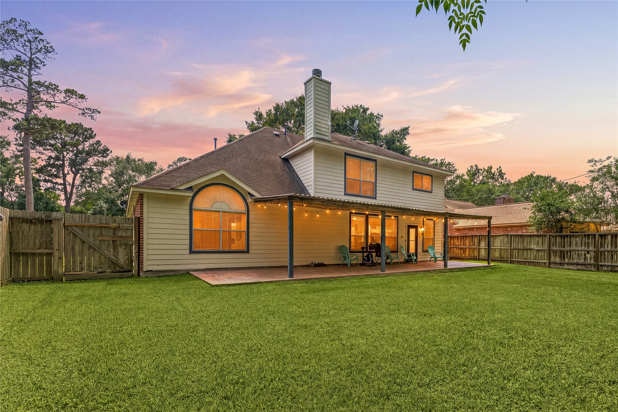 19726 Teller Boulevard Spring, TX 77388 - Photo 22 of 24 This stunning view showcases the rear of the home, where a large covered patio invites you to enjoy peaceful evenings overlooking the expansive, lush green lawn. The home's architectural charm is on full display with its warm exterior, soaring rooflines, and glowing windows that create a welcoming atmosphere. Fully fenced for privacy and framed by mature trees against a beautiful sunset sky, this outdoor space is the perfect backdrop for relaxation and entertaining.