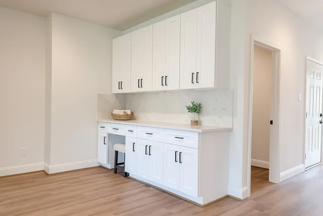 a white kitchen with granite countertop a stove a sink and white cabinets with wooden floor