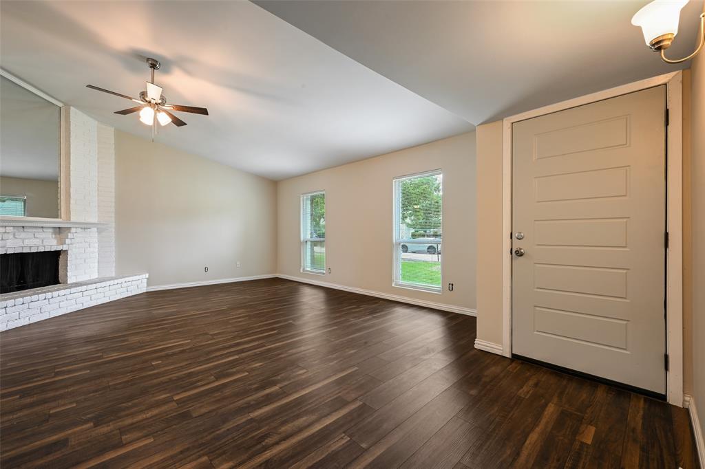 7318 Emory Oak Lane Dallas, TX 75249 - Photo 23 of 28 Spacious living area featuring wood-finish flooring, a white brick fireplace with mantel, and a vaulted ceiling with a ceiling fan
