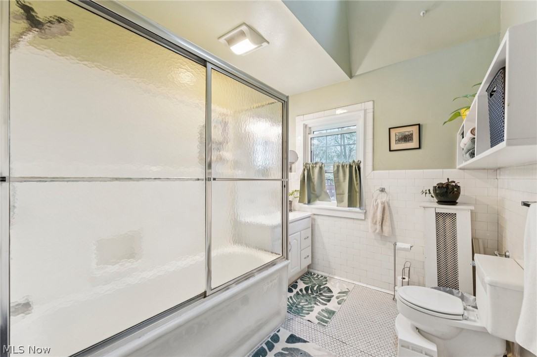2925 East Overlook Road Cleveland Heights, OH 44118 - Photo 22 of 48 This bathroom features a shower-over-bath with sliding glass doors, a window providing natural light, and classic white subway tile wainscoting