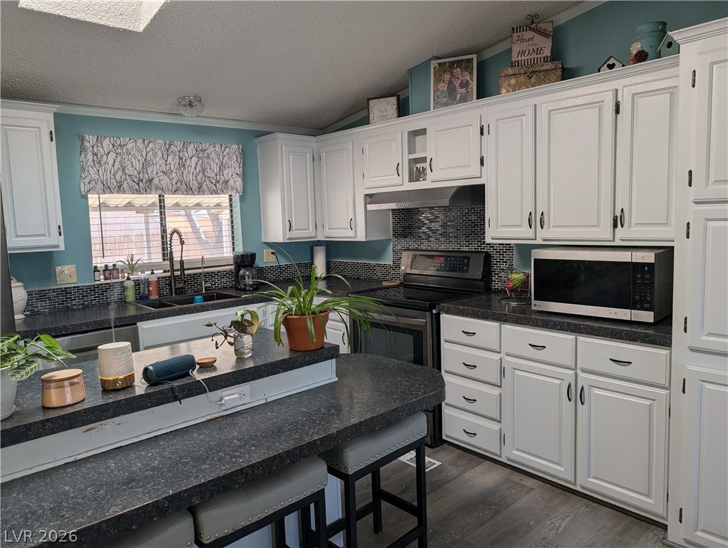 320 6th Street Panaca, NV 89042 - Photo 9 of 31 Kitchen with white cabinetry, stainless steel microwave, dark countertops, and tasteful backsplash