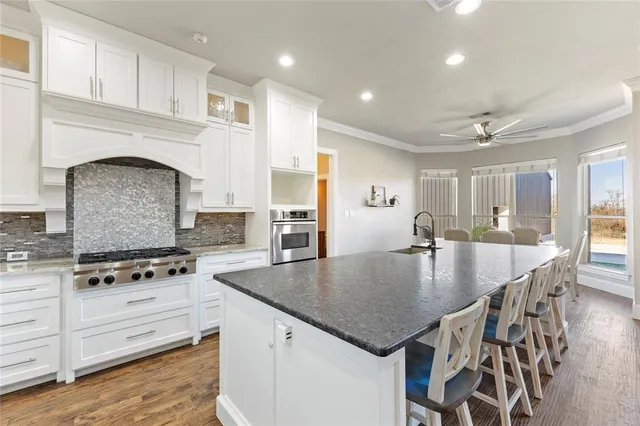 an open kitchen with granite countertop a stove top oven a sink dishwasher and white cabinets with wooden floor
