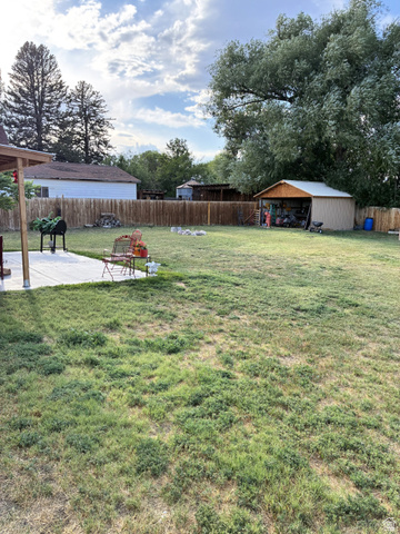 547 East 2000th Street North Vernal, UT 84078 - Photo 46 of 50 Expansive backyard featuring a large concrete patio, wood privacy fencing, a storage shed with an overhang, and mature trees