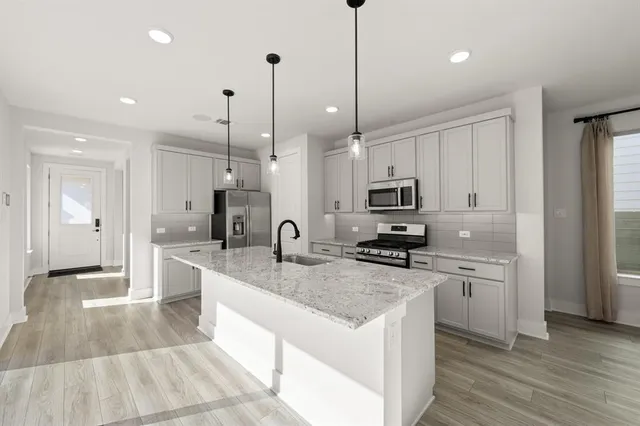 a kitchen with stainless steel appliances granite countertop a sink a stove a refrigerator and white cabinets