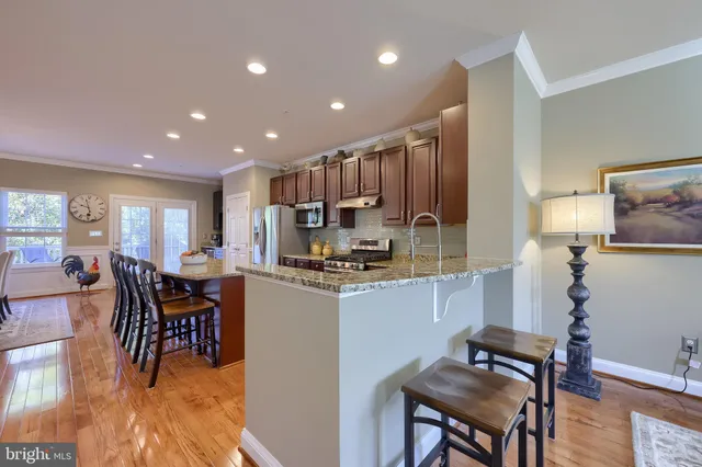a kitchen with stainless steel appliances kitchen island granite countertop dining table chairs and a refrigerator