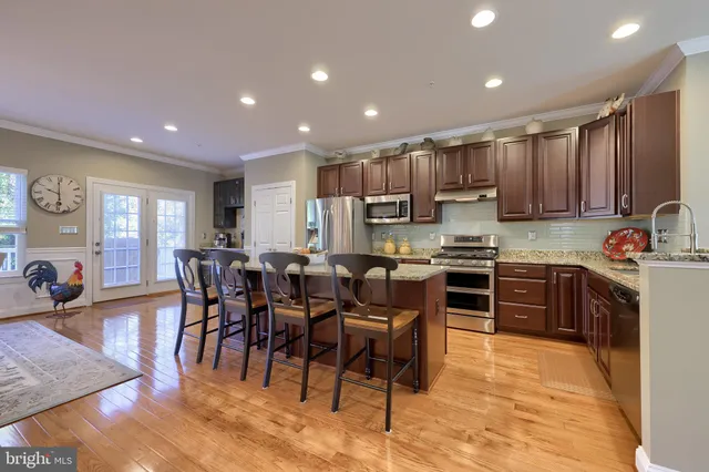 a kitchen with stainless steel appliances granite countertop a stove top oven a sink a dining table and chairs with wooden floor