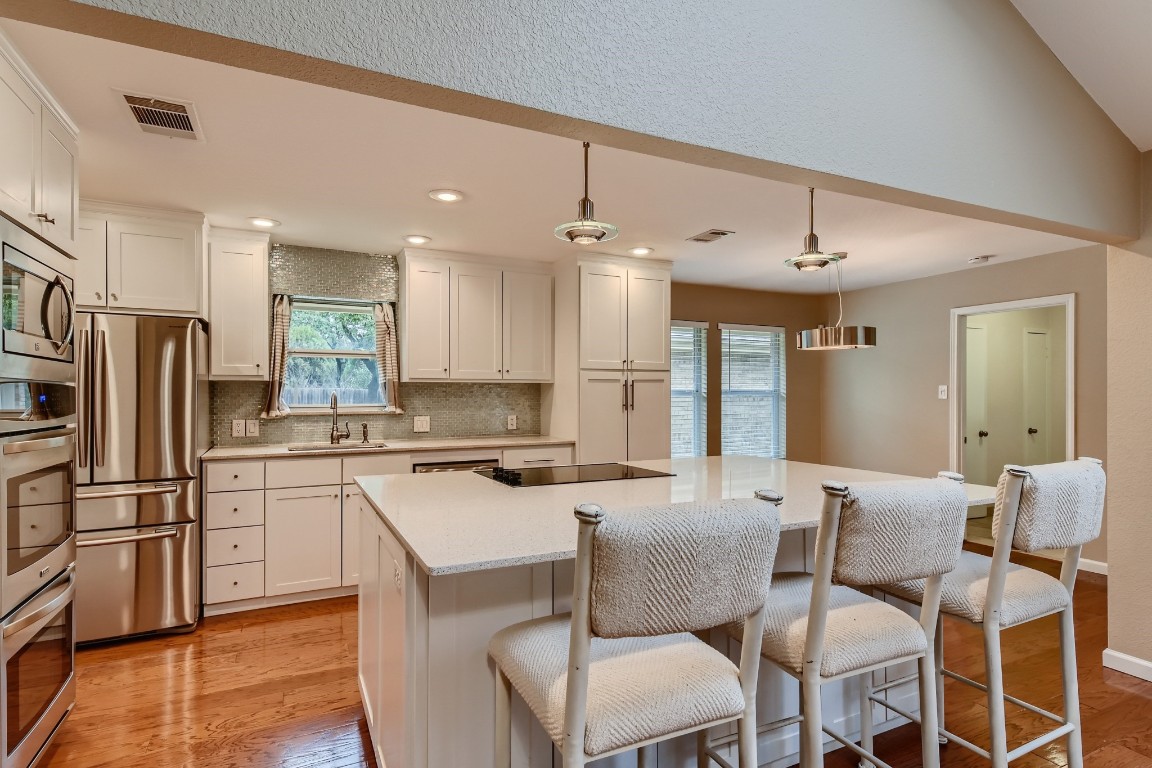 a kitchen with stainless steel appliances kitchen island granite countertop a dining table chairs refrigerator and sink